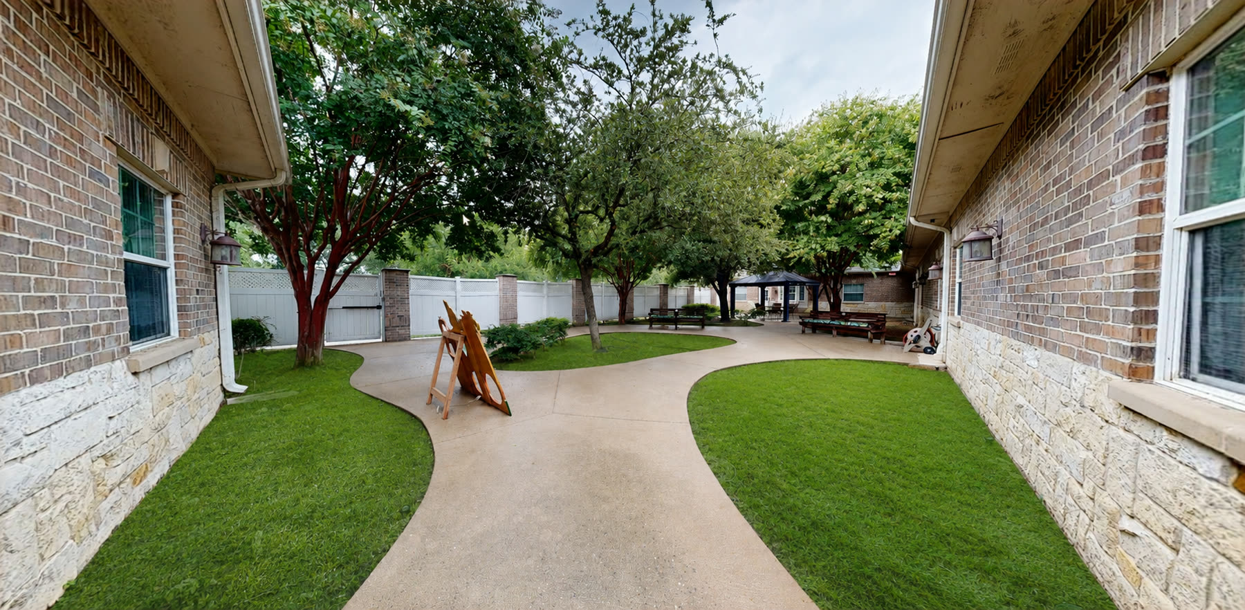 Secure outdoor courtyard with walking paths, benches, and shade trees at Magnolia Memory Care of Flower Mound